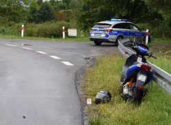 Na drodze widoczny skuter z uszkodzeniami, w tle oznakowany radiowóz policyjny