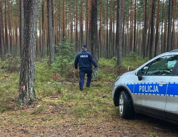policjant idzie przez las, w tle radiowóz