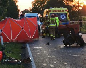 miejsce śmiertelnego wypadku, uszkodzony ciągnik i motocykl, w tle funkcjonariusze straży pożarnej i karetka pogotowia