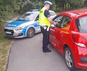 policjant stojący przy czerwonym samochodzie w tle radiowóz