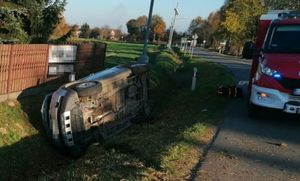 samochód leży na boku w rowie, obok na drodze stoi wóz strażacki