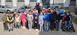 dzieci i policjant na wspólnym zdjęciu, w tle radiowozy i budynek