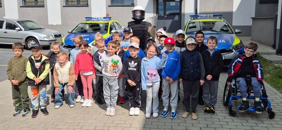 dzieci i policjant na wspólnym zdjęciu, w tle radiowozy i budynek