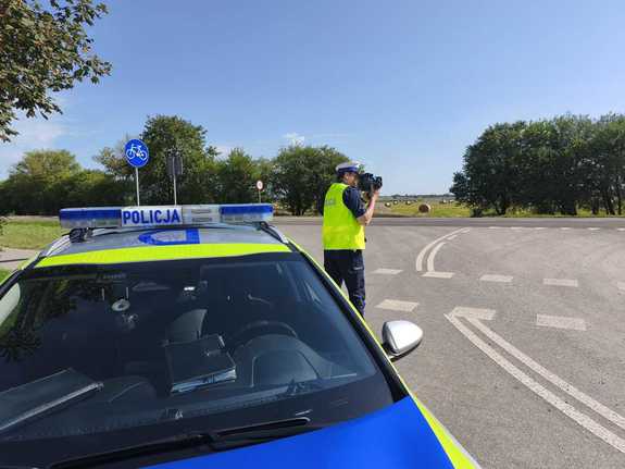Policjant sprawdza miernikiem prędkość pojazdów , obok radiowóz