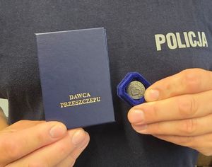 policjant trzyma w dłoniach legitymację i odznaczenie dawcy przeszczepu