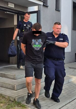 umundurowani policjanci prowadzą zatrzymanego mężczyznę do radiowozu