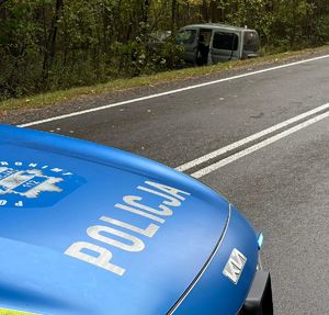 na pierwszym planie maska radiowozu, w tle uszkodzony samochód w przydrożnym rowie