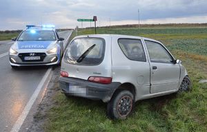 uszkodzony pojazd na poboczu drogi, obok na jezdni radiowóz policyjny