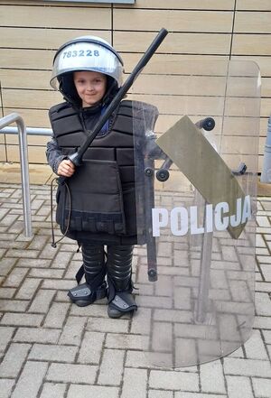 chłopczyk pozuje do zdjęcia w kasku, kamizelce i z tarczą policyjną