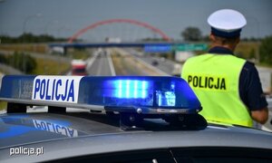 policjant stoi obok radiowozu i patrzy na drogę