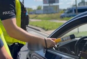 fragment zdjęcia z przeprowadzanej kontroli drogowej, policjant przeprowadza badanie trzeźwości kierowcy