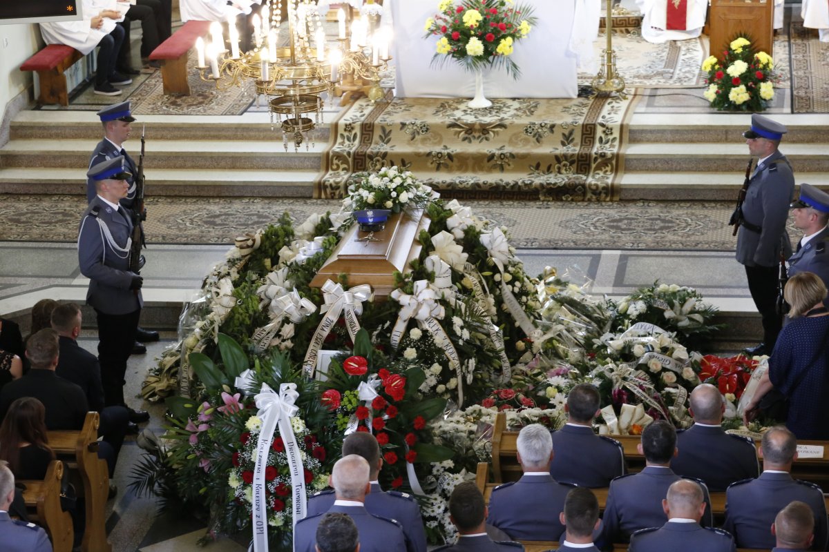 Wnętrze kościoła, trumna z ciałem Wnętrze kościoła w środku zdjęcia  trumna z ciałem sierż. szt. Tomasza Iwańca otoczona wieńcami.  Po obu stronach zdjęcia policjanci uczestniczący w pogrzebie.